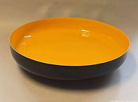 Top angled view of yellow-interior black-exterior footed bowl
