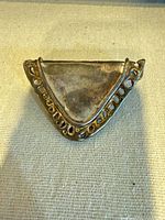 Front view of triangular sterling silver brooch showing decorative openwork border