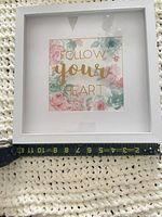 Front view of white square shadow box frame with floral art and gold text