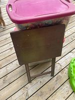 Front view of folded wooden TV dinner table leaning against storage bin