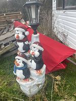 Full view of stacked penguin sculpture with solar lamp and red umbrella nearby