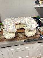 Both U-shaped pillows stacked showing colourful sea-creature print and grey floral-heart pattern