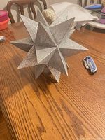 Overall view of silver glitter plastic multi-point star tree topper on table