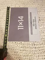 Front of packaged Studio Décor 11x14 glass showing size label and tape measure for scale