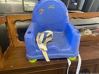 Front view of blue plastic toddler booster seat with white straps and green feet