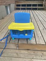 Front view of blue booster seat with yellow tray attached on wooden deck
