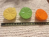 Three closed containers in yellow, green, orange with measuring tape showing under 5 inches