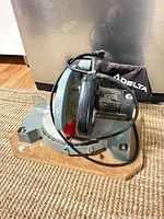Left side view of Delta compound miter saw on plywood base showing blade guard and cord