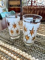 Two frosted glass tumblers with gold starbursts on woven mat