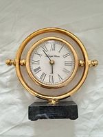 Front view showing gold circular case, white Roman numeral dial, marble base