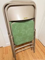 Four Samsonite folding chairs stacked, showing beige metal frames and green vinyl seats