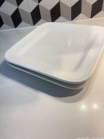 Two stacked white square porcelain platters on countertop