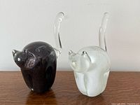 Front view of both glass cat sculptures on wooden surface