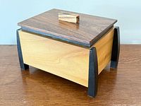 Oblique view showing walnut lid with zebrawood pull, light body wood, black legs