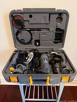 Full view of open carry case showing spin saw, angle grinder adapter, side handles, abrasive disc, and accessories