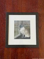 Framed pastel painting showing Siamese cat by window, white mat, dark wood frame