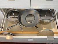 Drawer view showing three saucepans, one wok-style pan, and three lids