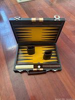 Open backgammon case showing interior surface, dice cups, checkers, dice and exterior hardware