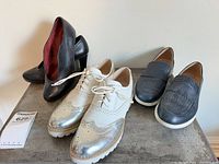 All three pairs of shoes displayed together: navy loafers, white/silver brogues, black pumps
