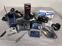 Group shot showing all items including Casio TV, Konica, Samsung and Mustek cameras, Vivitar flash, dock, cables and cases