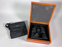 Binoculars inside open wooden case next to carry bag