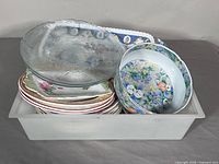 Bin containing stacked plates, bowls and clear glass platter