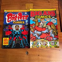Both Big Ass Comics issues laid side by side on table, full view front covers