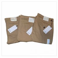 Three folded tan chinos with hangtags visible