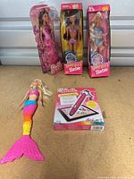 Front view of all five items showing three boxed dolls, loose mermaid doll and boxed Fashion Creator Pen