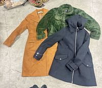 Top view of three jackets laid out: camel long coat, green faux fur, navy hooded coat