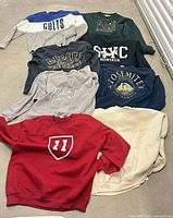 Eight assorted large men’s sweatshirts laid out on floor