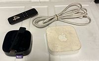 Top view of Apple TV unit, Roku player with stick, Fire TV remote, power cord