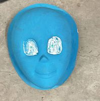 Front view of blue plaster face mask, shows full shape, color, and painted eye areas