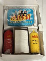Box interior showing sealed playing cards tin and wrapped red and yellow shakers
