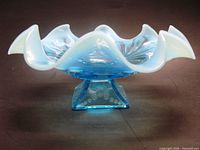 Side view of blue opalescent ruffled bowl on square pedestal base