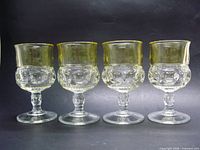 Four clear pressed glass goblets with yellow rims, front view