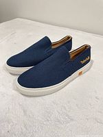 Full view of both navy blue slip-on shoes, left side angle, shows fabric texture and white soles