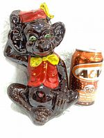 Front view of ceramic monkey coin bank beside A&W can for scale