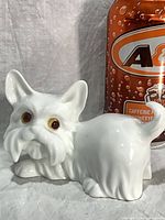 front view of white bone china terrier figurine beside soda can for scale