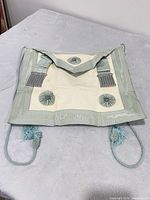 Front view displaying blue silk trim, cream panel, rosettes, bullion tassels, cord ties