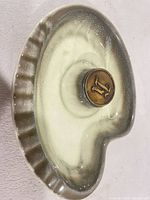 Top view of kidney-shaped green and cream glazed pottery ashtray with central steel monogram disk