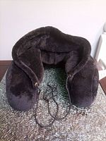 Front view of black plush neck pillow with hood and drawstring