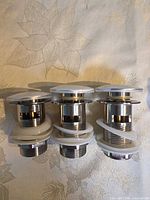 Front view of three chrome pop-up drain wastes with white protective rings
