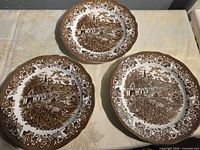 Group of three identical brown transferware dinner plates on table