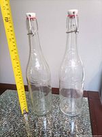 Front view of two clear swing-top bottles beside measuring tape showing height