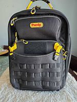 Front view showing Purdy logo, exterior pockets, MOLLE loops, yellow buckles, lockable zippers