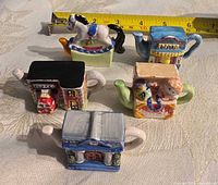 Five miniature ceramic teapot figurines, top view with tape measure for scale