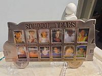 Front view of pewter-finish metal school bus frame showing 12 labeled photo slots