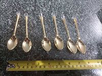 Six gold-tone teaspoons aligned with measuring tape showing length