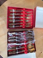 Open boxes showing 6 forks in top tray, 6 spoons in bottom tray, original packaging
